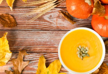 Seasonal pumpkin soup, autumn leaves and pumpkins on a wooden background. Copy space. Top view.