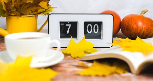 The flip clock shows 7 o\'clock in the morning. Early awakening in autumn. A book and a cup of hot coffee in the foreground in blur. Close-up.