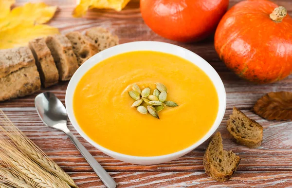 Delicious pumpkin soup, pumpkins and rye bread on a wooden background. Close-up.