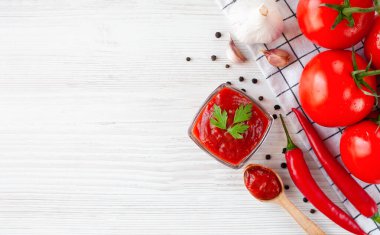 Ketchup and ingredients: tomatoes, garlic and red hot pepper on a wooden white background. Close-up. Top view. Copy space.