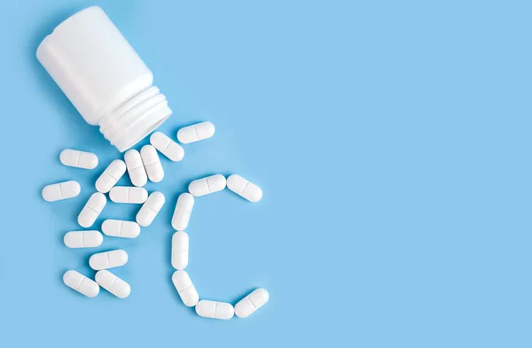 The white pills are in the shape of the letter C on a blue background. Taking vitamins. Healthy lifestyle concept. Close-up. Copy space.