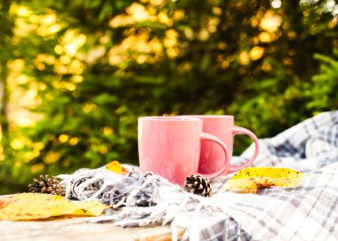 Two cups of coffee and checkered plaid on wooden bench. Autumn picnic outdoor. Close-up.