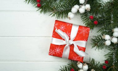 Festive New Year or Christmas composition with gift box and fir branches on the white wooden background. Close-up. Top view. Copy space.