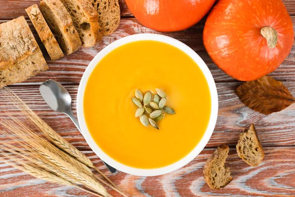 Pumpkin cream soup with rye bread and pumpkins on a wooden background. Seasonal vegetables menu. Top view. Close-up.