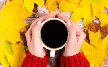 Kadın elleriyle sonbahar kompozisyonu, bir fincan sıcak aromatik kahve ve sonbahar sarı yaprakları. Flatlay. Üst Manzara. Seçici odak.