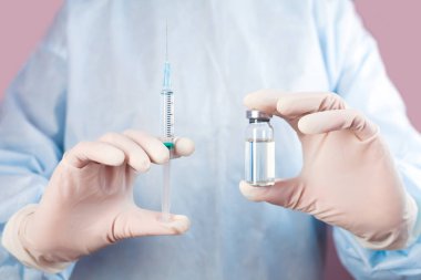 Doctor or nurse in medical mask and in protective gloves holds syringe and medical injection in hands. Influenza and coronavirus vaccination. Close-up.
