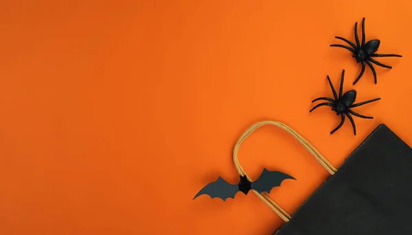Paper black package, bat and spiders on orange background. Halloween shopping and sale concept. Flatlay composition. Banner. Place for text.