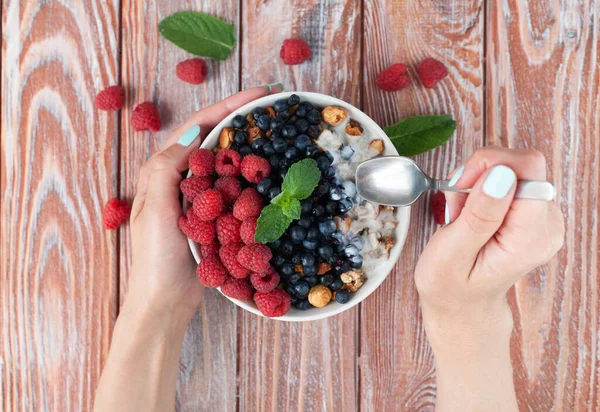 Women\'s hands holds spoon and a bowl of muesli and fresh berries. Healthy breakfast. Top view.