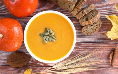 Balkabaklı sonbahar kompozisyonu, balkabağı kremalı çorba ve ahşap zemin üzerinde çavdar ekmeği. Mevsimlik sebzelerden sağlıklı yiyecekler. Üst Manzara. Yakın plan..