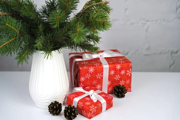 テーブルの上のスタイリッシュな白い花瓶にクリスマスギフトボックスとスプルースの枝 新年とクリスマスへの贈り物 お祭り気分 スペースのコピー — ストック写真