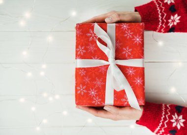 Kırmızı Noel kazaklı bir kadının elleri beyaz kurdeleli kırmızı hediye kutusunu tutuyor. Üst Manzara. Yakın plan. Tatil hediyesi. Noel ve Yeni Yıl konsepti. Mesaj için yer. Pankart.