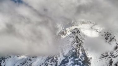 Yüksek irtifa, kayalık dağ zirvesi. Kış mevsiminde göz kamaştırıcı ve görkemli dağ kütleleri. Dik ve dikey yamaçlar. 8K HDR zamanının bulutlu hareketleri. Şimdi dağ yamacı ve vadiyi kaplıyor. 8K 7680x4320 4320p.