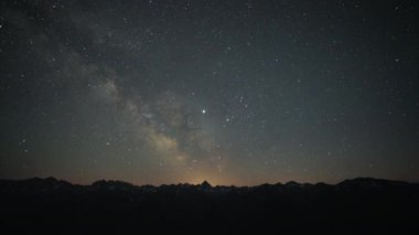 Gece gökyüzünde Samanyolu yıldızları. Yıldızlı gökyüzünün dağların üzerindeki zaman aşımına uğramış videosu. Gece yıldızlı gökyüzü ve ön plandaki dağlar. Gerçek renkler. 8K 7680x4320 4320p.
