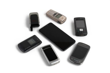 Beyaz arka planda izole edilmiş eski cep telefonlarıyla çevrili yeni modern akıllı telefon.