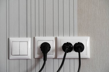 Beyaz elektrik prizi ve gri bir duvarda iletken kablolar ve prizler var..