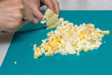 Bir kadın yeşil bir panoda bayram salatası için haşlanmış yumurtayı bıçakla kesiyor. Sadece elleri görünüyor..