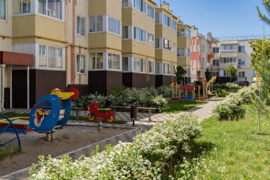 Yeşil bitkileri olan evler ve çocuklar için eğlence alanları arasında rahat bir avlu. Kozalaklar, çalılar ve çiçekler arasında açık hava eğlencesi için harika bir yer..