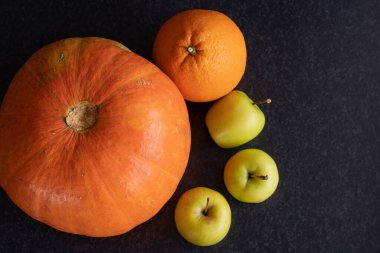 Güzel olgun balkabağı, portakal ve elmalar koyu bir arka planda.