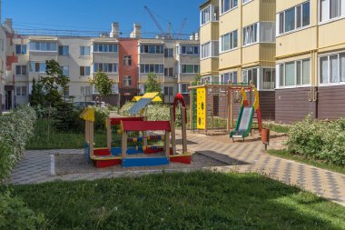Yeşil bitkileri olan evler ve çocuklar için eğlence alanları arasında rahat bir avlu. Kozalaklar, çalılar ve çiçekler arasında açık hava eğlencesi için harika bir yer..