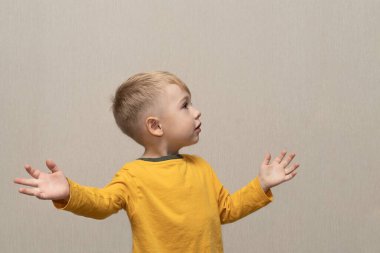 Sarı tişörtlü, sarışın, Avrupalı, 3 yaşında, gri arka planda izole bir çocuk. Reklam planı için iletişim kuruyor. Seçici odak noktası ve bulanık arkaplanı olan yakın plan..