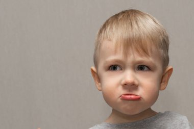 Yakışıklı sarışın bir çocuğun yüzü. 3 yaşında. Yüzünde sinirli ve kaprisli bir çocuğun yüz ifadeleri ve duyguları var..