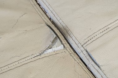 Kanepenin üzerinde dikişleri olan yırtık, hakiki bej bir deri. Eski hasarlı deri kanepe, restorasyon için büyük bir delik. Cilt yenileme.