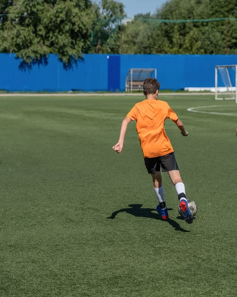 The boy loves to play football, trains with the ball on the artificial turf and scores a goal. The boy plays football.