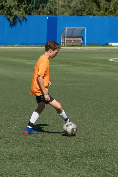 The boy loves to play football, trains with the ball on the artificial turf and scores a goal, the boy plays football.