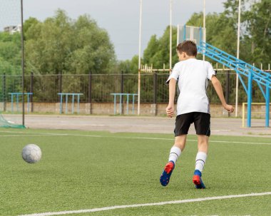 Çocuk futbol oynamayı, yapay sahada topla antrenman yapmayı ve gol atmayı seviyor. Çocuk futbol oynuyor..