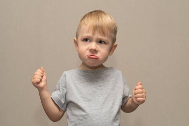 Gri tişörtlü hoş bir çocuk. 3 yaşında. Gri arka planda izole edilmiş. Öfke ve öfke gösteriyor..