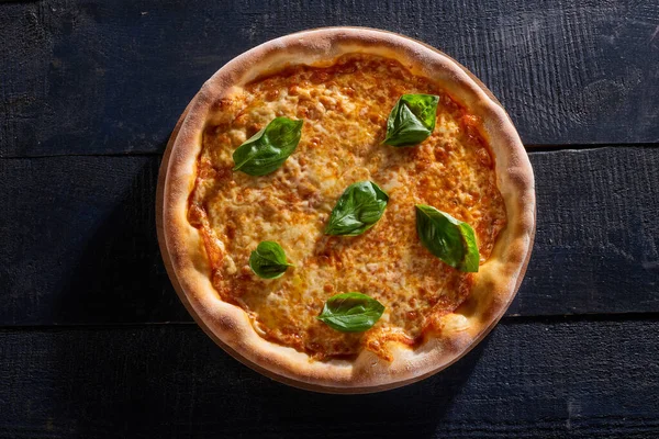 Fesleğenle süslenmiş peynirli pizza. Koyu ahşap arka plan manzaralı.
