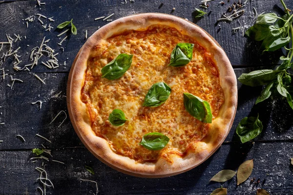 Fesleğenle süslenmiş peynirli pizza. Koyu ahşap arka plan manzaralı.