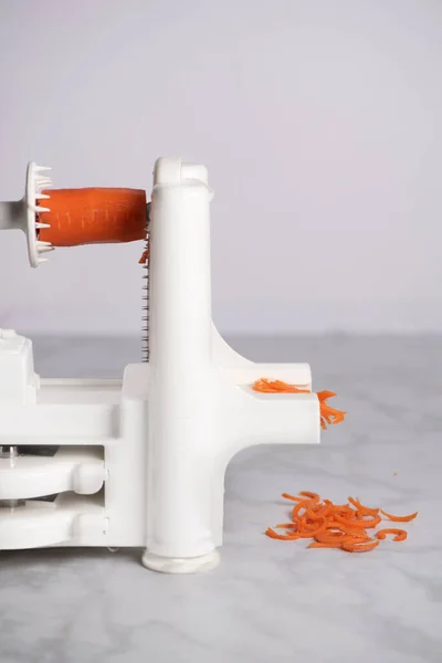 Davis, CA, USA, April 10, 2022. Spiralizer 7-Blade Vegetable Slicer, Veggie Pasta Spaghetti Maker for Keto/Paleo/Non-Gluten diet, shredding a carrot root against white background