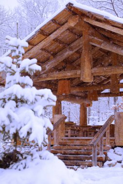 Bir ahşap kulübe, karla kaplı bir ormanda kar yağan bir çardak gibidir.