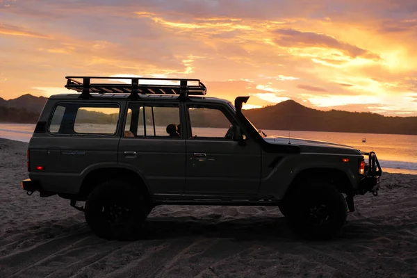Gün batımında güzel bir sahilde 4X4 numaralı araba. Offroad arabaları ve yaşam tarzı, kişisel gelenekler. Altın saat