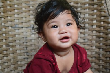 Kahkahalar atan bir sandalyede oturan kahverengi gömlek giyen Asyalı bir çocuğun gülümsemesi ve gülüşü.