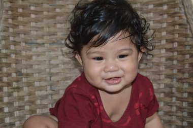 Kahkahalar atan bir sandalyede oturan kahverengi gömlek giyen Asyalı bir çocuğun gülümsemesi ve gülüşü.