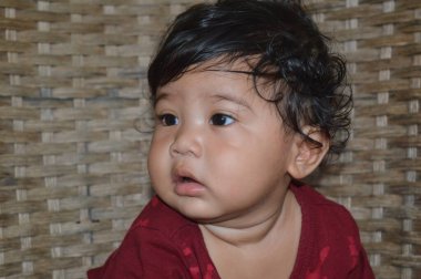 Kahkahalar atan bir sandalyede oturan kahverengi gömlek giyen Asyalı bir çocuğun gülümsemesi ve gülüşü.