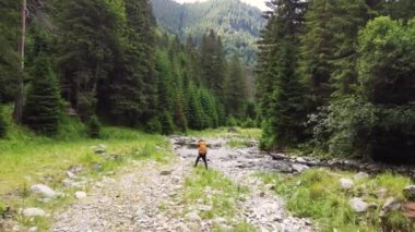 Back view of a tourist young man with a backpack travels through the forest near the river. young man equipped with tourist equipment hiking, lifestyle. active life mode, active rest. High quality 4k