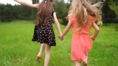 Sisters Hold Hands And Run In Slow Motion Through Beautiful Meadow, They Look Back Over Their Shoulders And Smile. High quality FullHD footage
