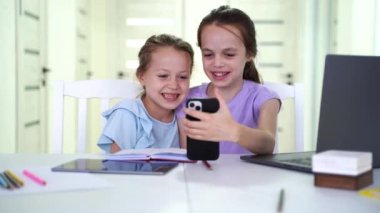 happy small friends playing online mobile games or using funny apps on smartphones together indoors. Addicted to tech diverse little children foster sisters having fun at home. High quality 4k
