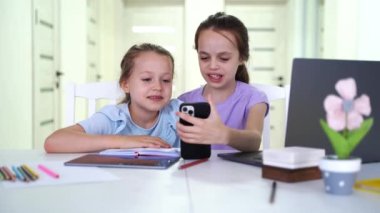 happy small friends playing online mobile games or using funny apps on smartphones together indoors. Addicted to tech diverse little children foster sisters having fun at home. High quality 4k