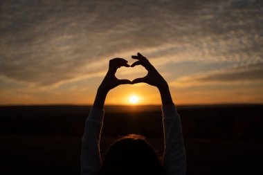 Gün doğumunda ya da gün batımında güneş gökyüzüne karşı yapılmış el kalp şeklinde bir siluet. Yüksek kalite fotoğraf