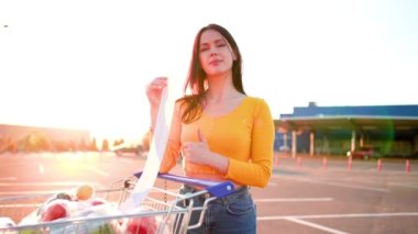 Otoparktaki kameraya bakan genç bir kadın hipermarketten alışveriş yaptıktan sonra el hareketi gösteriyor. Yüksek kalite 4k görüntü