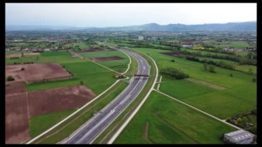 Hava aracı görüntüsü. Tarımsal tarlalar ve yeşil kırsal alanların arasından geçen beyaz araba, takip eden araçlar. Yüksek kalite 4k görüntü