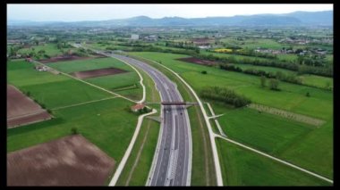 Hava aracı görüntüsü. Tarımsal tarlalar ve yeşil kırsal alanların arasından geçen beyaz araba, takip eden araçlar. Yüksek kalite 4k görüntü