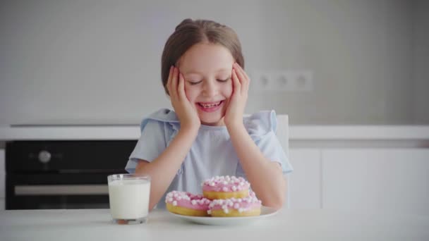 ポートレート幸せな子供6歳は釉薬で食欲をそそる甘いデザートを食べます 陽気な白人の少女は甘いドーナツを食べる 子供の口の近くに甘いペストリーを食べている — ストック動画