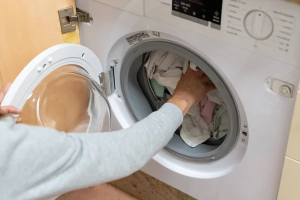 Woman's arm filling the washing machine drum. Concept of energy consumption, high price of electricity, household chores, housewives, turning on the washing machine.