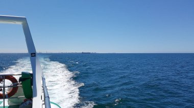 Arkasında deniz, mavi gökyüzü ve kıyı olan bir teknenin arka görüntüsü. Kopya uzayı ile yatay görüntü. Tatil konsepti, yaşam tarzı, rahatlama ve doğa..