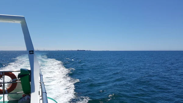Arkasında deniz, mavi gökyüzü ve kıyı olan bir teknenin arka görüntüsü. Kopya uzayı ile yatay görüntü. Tatil konsepti, yaşam tarzı, rahatlama ve doğa..